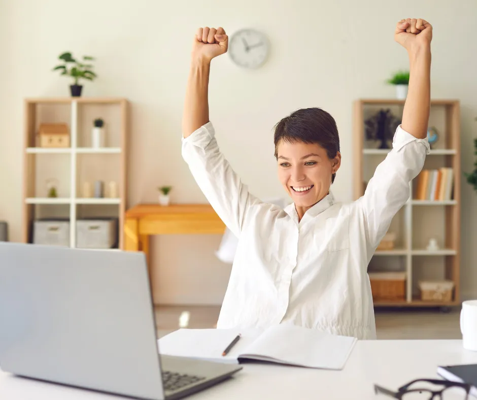Woman stretching her arms up in celebration at her desk